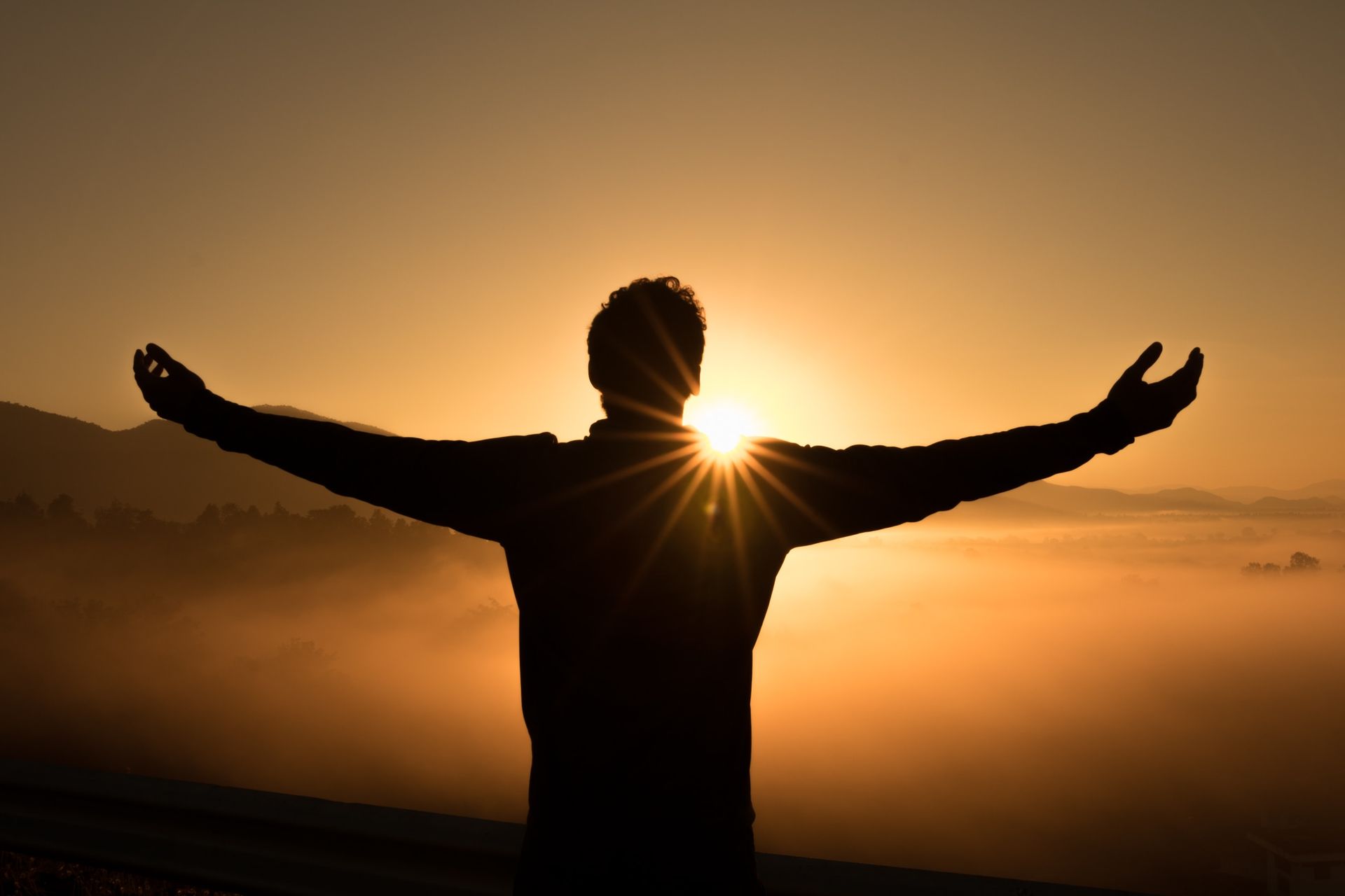 A figure with arms raised at sunrise